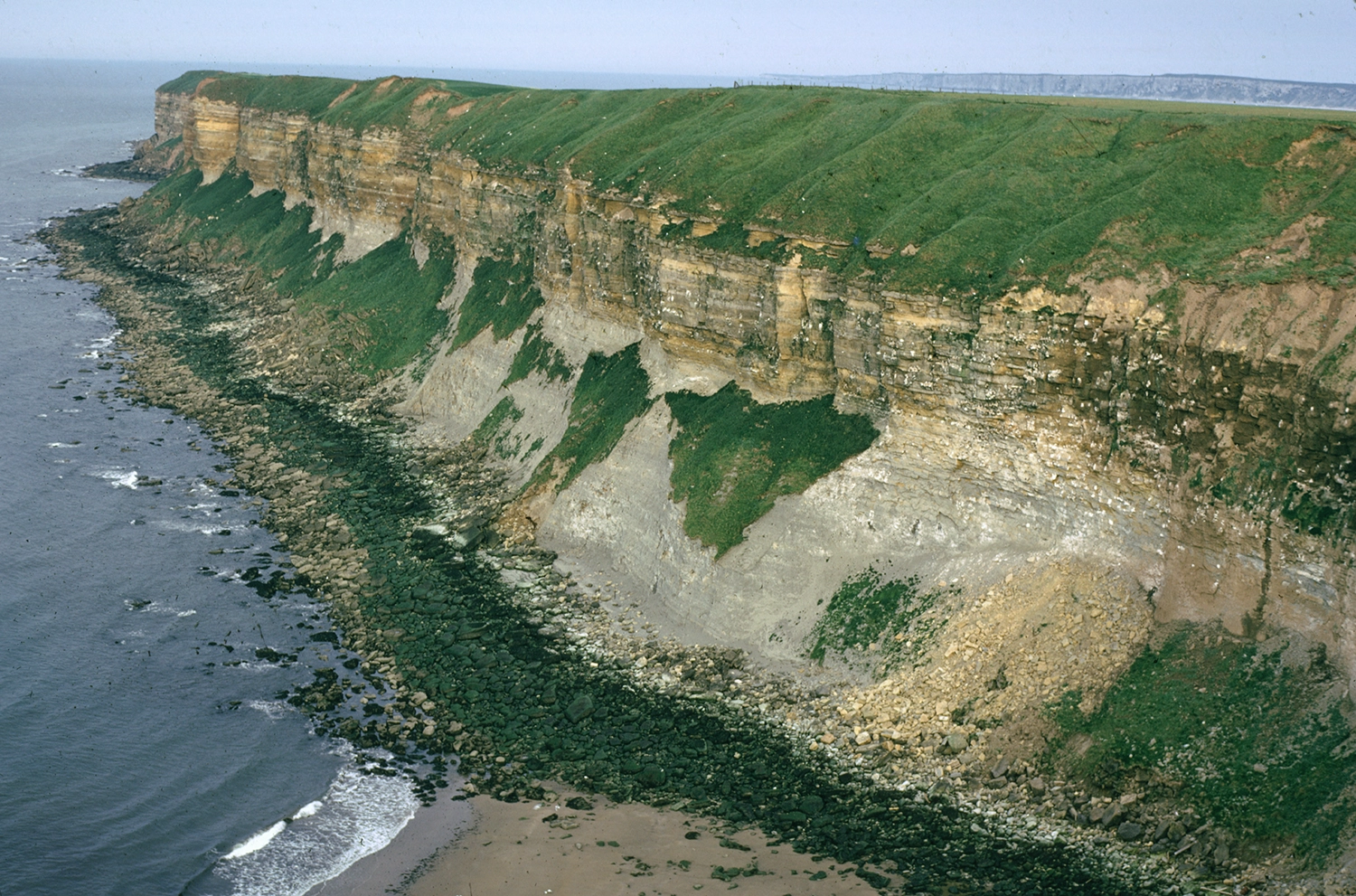 sea cliffs of a dark grey mudstone (Oxford Clay Formation) overlain by well bedded yellowish limestone (Corallian Group)