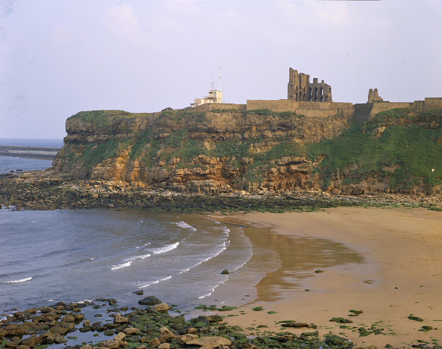ruined priory on top of a cliff, with waves breaking on a beach
