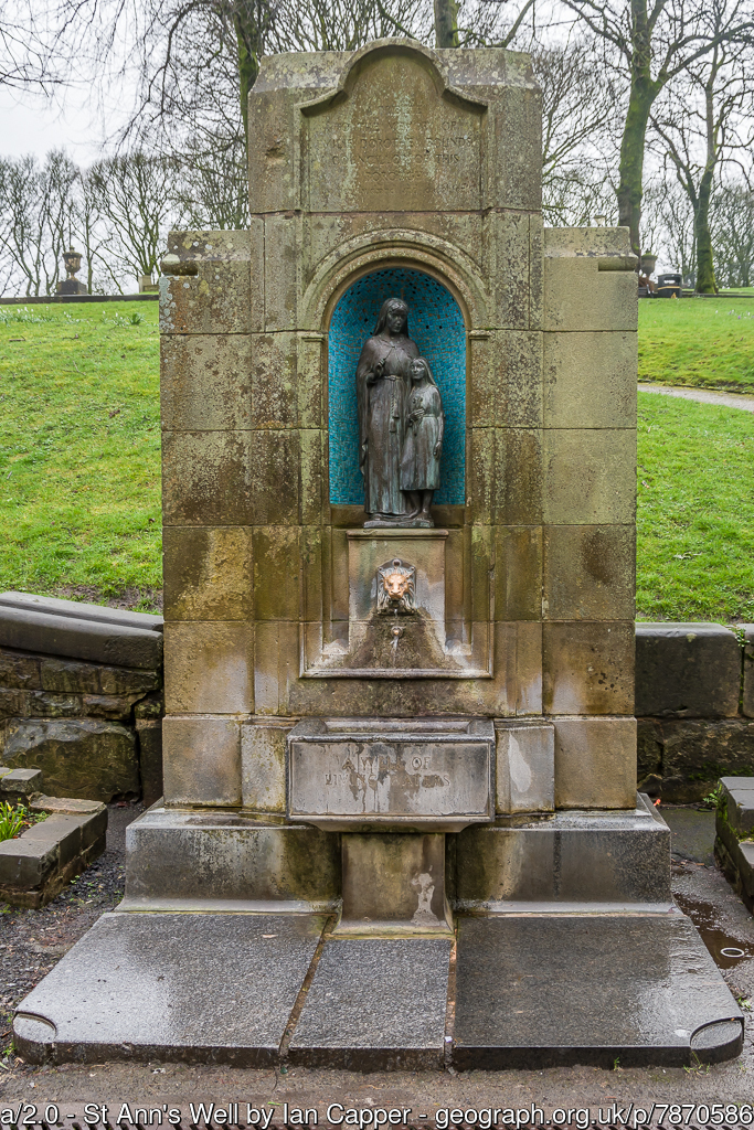 A stone edifice with a statue of St Ann and the Virgin Mark. a lion's head and a basin. Water pours out of the lion's head into the basin.