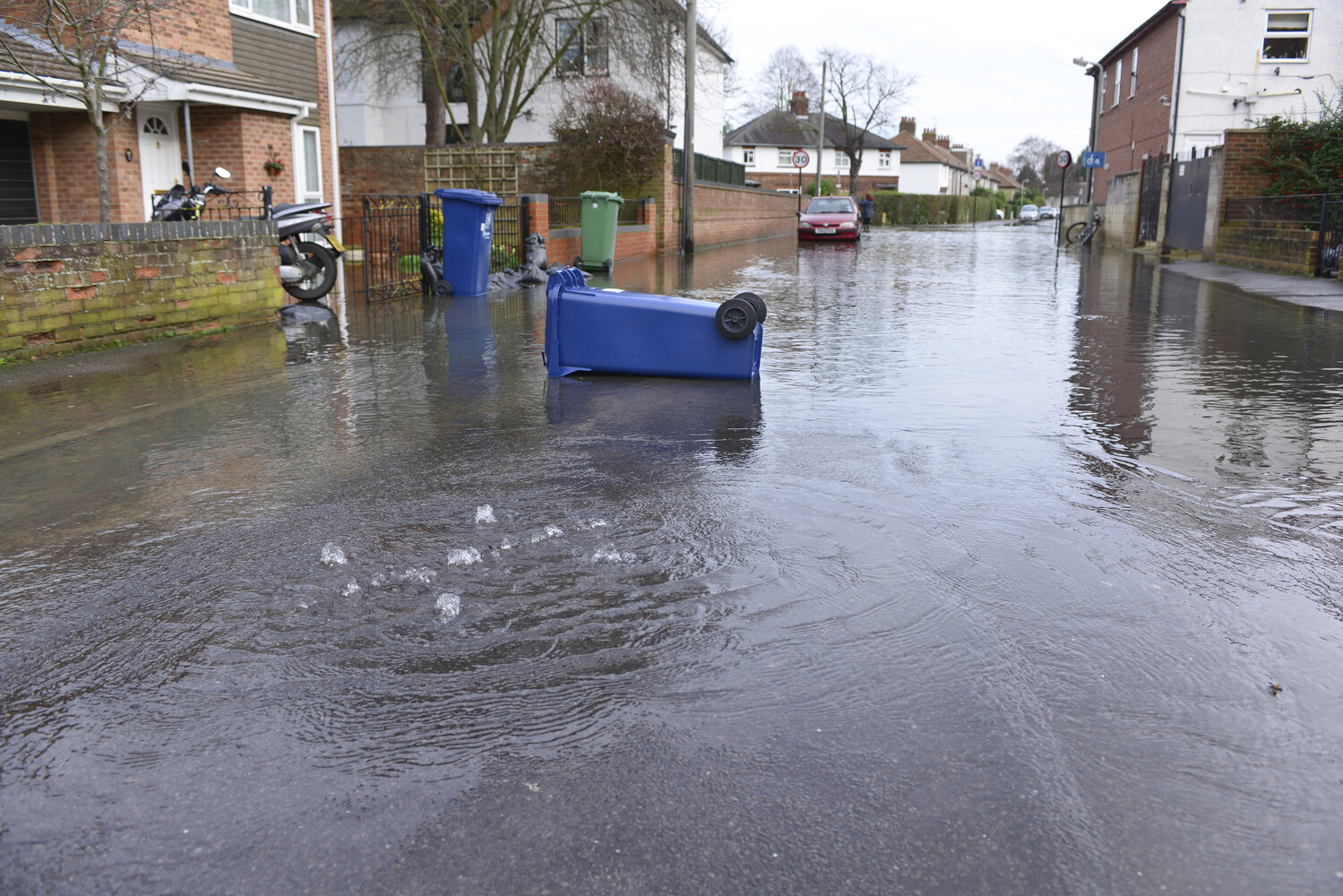 an overturned blue wheelie bin lies in a flooded street
