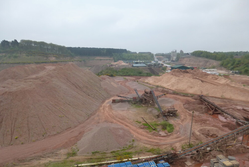 A quarry dug into orange-coloured sand, with machinery and blue containers at the bottom of the quarry