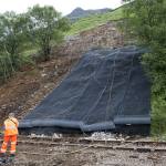 Debris pathway downslope, partly netted. Debris on the railway line has been cleared and the line is in the process of being repaired.