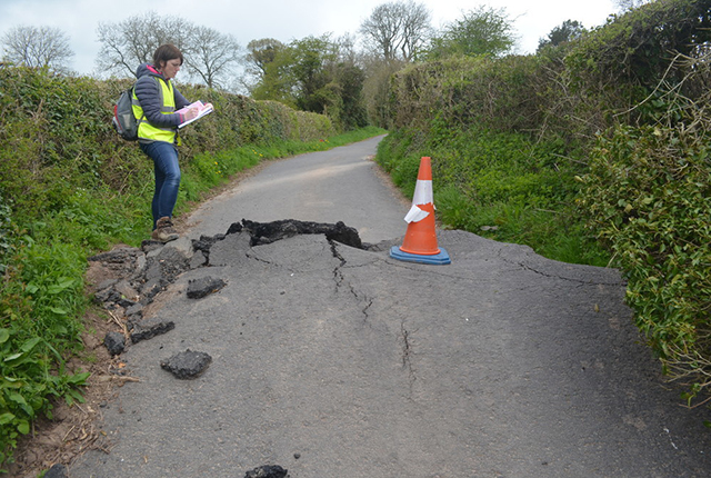 The road has buckled up under compressional forces as the ground beneath it moved downslope.