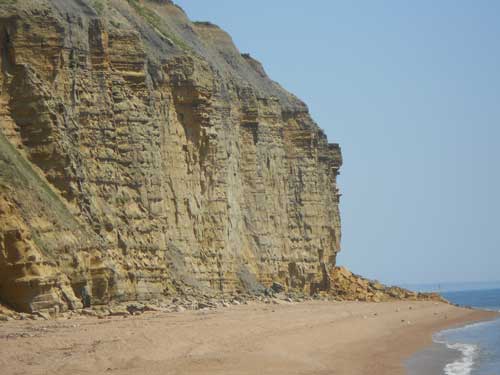 Eroding piles of rock debris along the base of the Jurassic sandstone cliffs at Burton Bradstock are telling signs of continual erosion by landslides. Taken 25 July 2012.