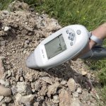 A handheld monitoring device is being pressed against a pile of soil and gravel