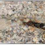 A close-up picture of speckled pink and grey crystalline rock with a line of darker material running through it.