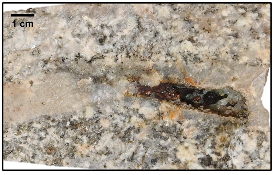 A close-up picture of speckled pink and grey crystalline rock with a line of darker material running through it.
