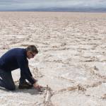 A geologist kneeling on a wide, white expanse of a salt flat in Argentina