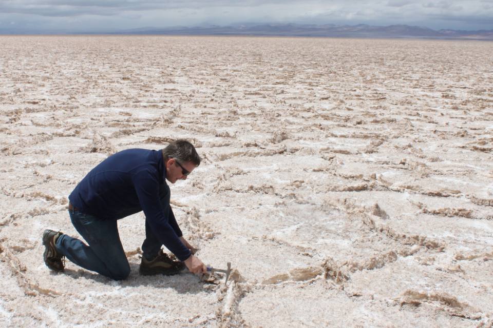 A geologist kneeling on a wide, white expanse of a salt flat in Argentina