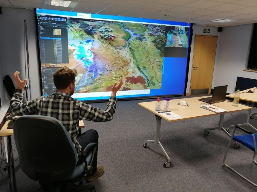 A man sitting in front of a large screen showing a geological map