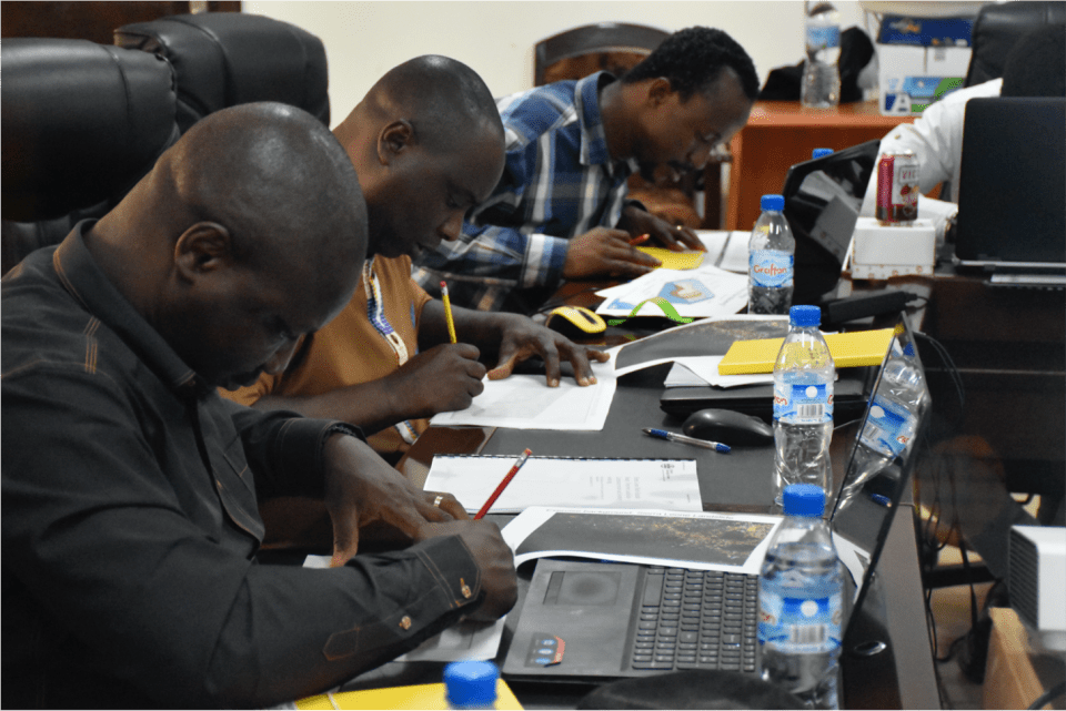 A group of students sat at computer terminals, drawing with pencils on pieces of paper
