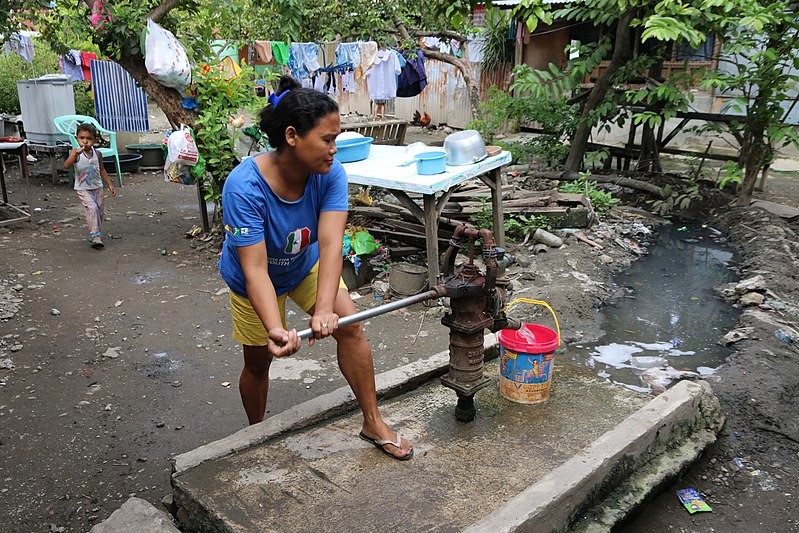 A wom,an pumping water from a public well in a street