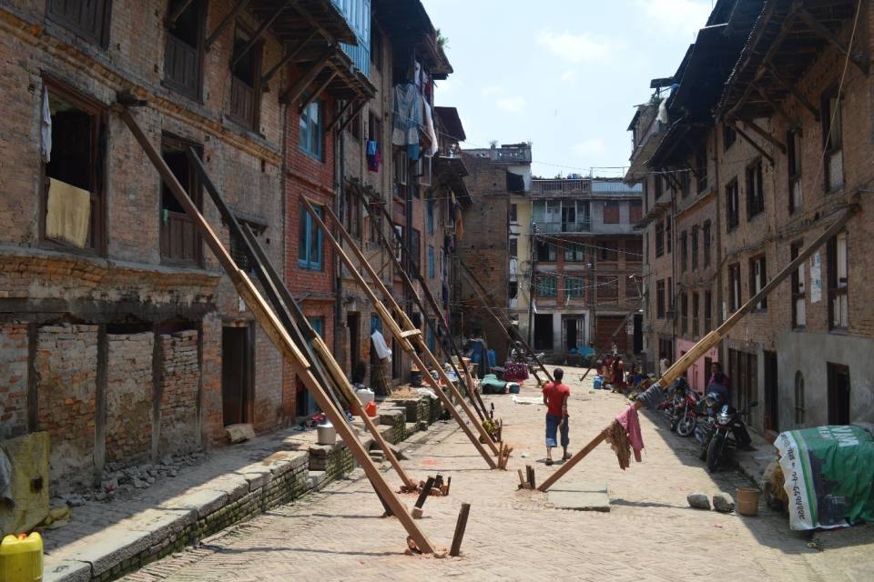 Buildings that have been damaged being shored up with long plans of wood in a nearly deserted street