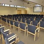 Chairs lined up inside a large room facing a smartboard on the wall at the far end