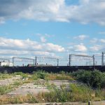 A large, unused, urban brownfield site with open land covered in cracked, overgrown concrete awaiting development in Leeds, England. © Adobe Stock, 282946502.