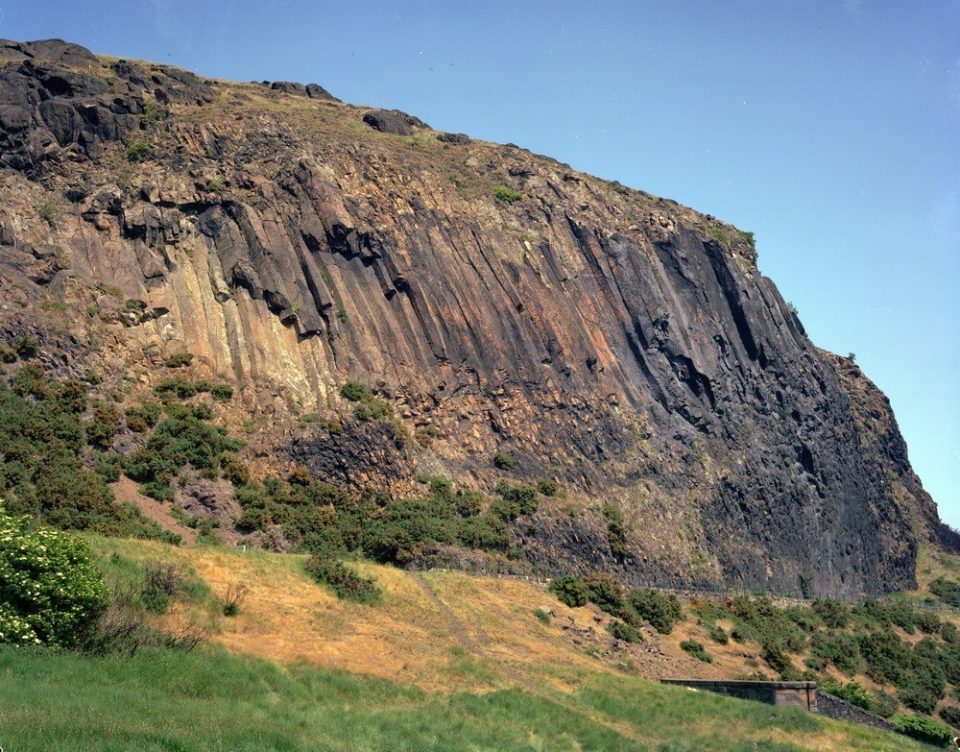 A high cliff formed of subvertical pillars or columns of brownish grey rock