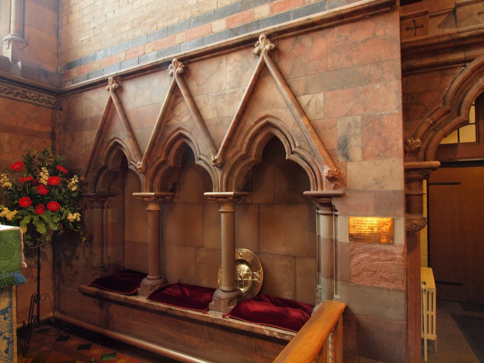 Three pointed-arched church seats (sedilia) made of pink labastr with red velvet cushions