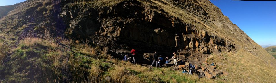 The side of a cliff with an exposure of rock being examined by people