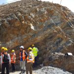 People in hi-vis vests and hard hats stood in front of layered, folded rocks