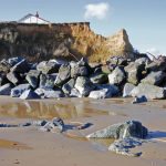 Large boulders in front of a sandy cliff with a building perched on top