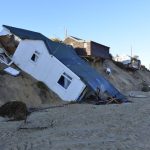 Seveal small buildings slumped down a small, sandy cliff above a beach