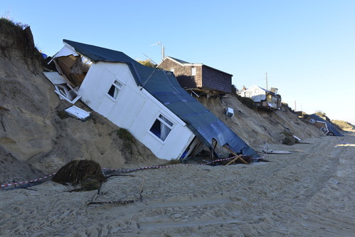 Seveal small buildings slumped down a small, sandy cliff above a beach