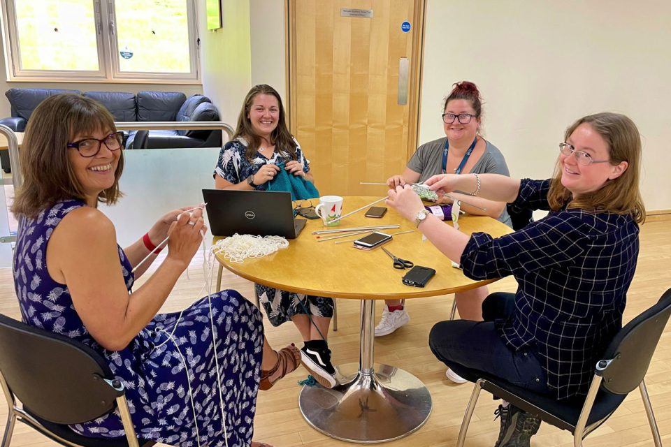 Four BGS staff members sitting at a table knitting