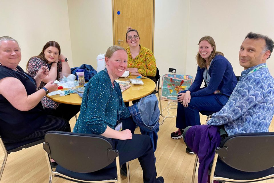 A grou of BGS staff memenbrs sat around a table mending clothes.