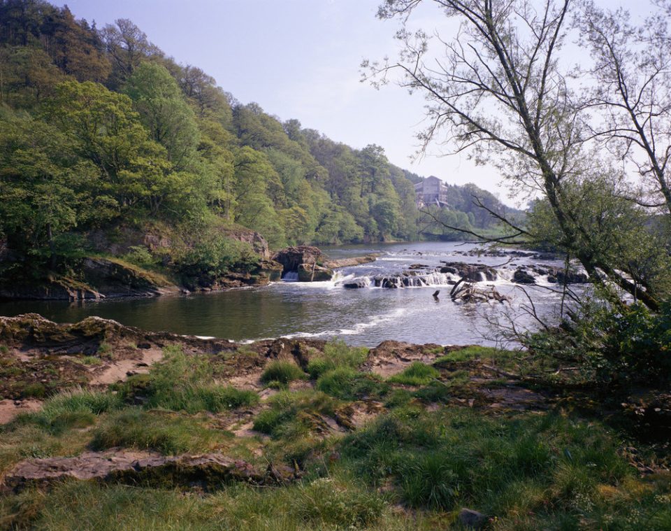 A river flowing through a shallow wooded gorge, with mine building in the backgroundgorge