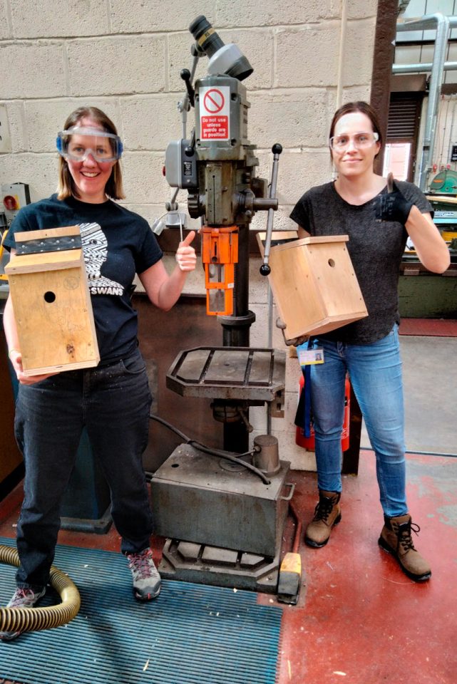 Two staff members wearing safety equipment holding bird boxes they have just made