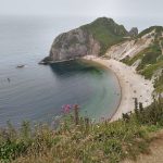 A view from a clifftop across a curved bay with a beach at the base of steep cliffs