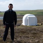 BGS geomagnetism team member Guanren Wang stands in front of a white hut