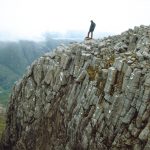 Columnar jointing on the side of a steep valley. A human figure stands on top.