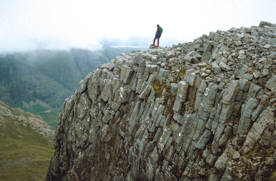 Columnar jointing on the side of a steep valley. A human figure stands on top.