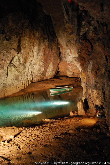 A pool of water in a cave with a boat on it, lit up from underneath