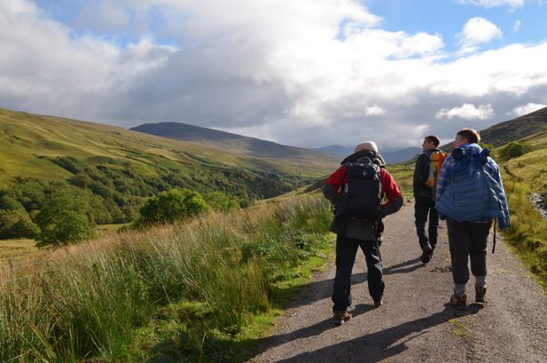 Three people walking along a path in a green valley