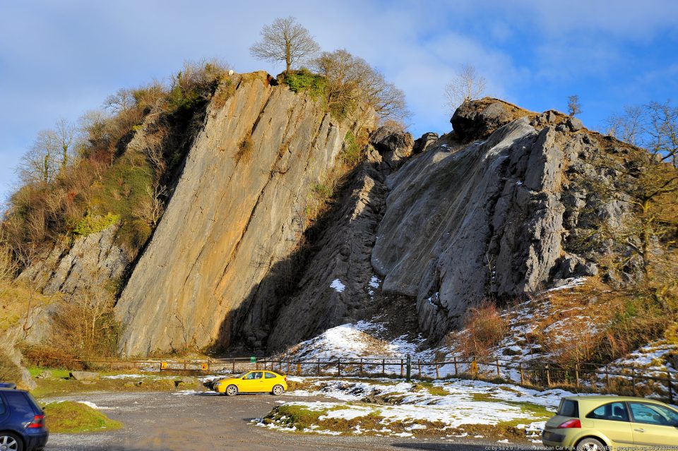 A steeply dipping blick of rock with a sheer vertival face, with some snow on it