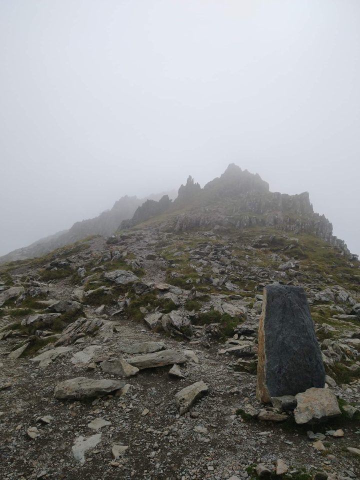 Grey outcrops of rock sticking up into the mist at the to of a mountain.