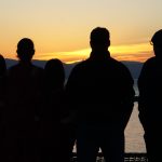 Silhouettes of five people standing watching the sun set over the sea