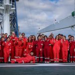 A group of people all wearing red jumpsuits on the deck of a ship