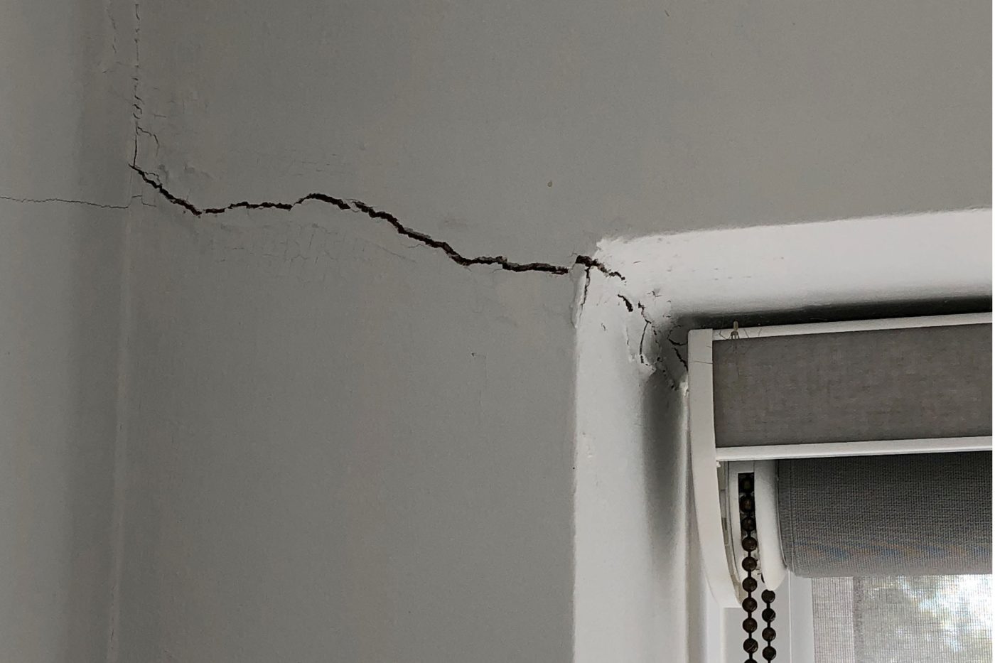 A large crack runs across a white wall to the corner of a window.