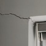 A large crack runs across a white wall to the corner of a window.