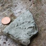 Small cube shapes in a grey fragment of rock with a 1 pence iece for scale. The cubes are about a third of the width of the coin.