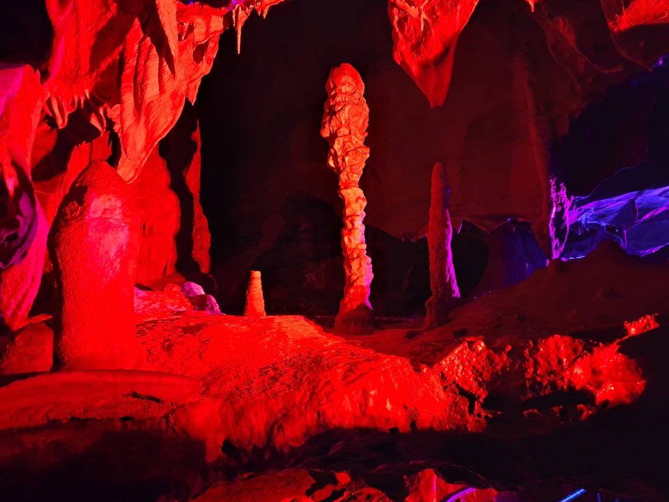 Columnar speleothems bathed in red artificial light in a cave.
