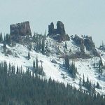 Two rock formations on top of a snowy hill. The one on the left is a square block; the one on the right resembles a pair of rabbit's ears