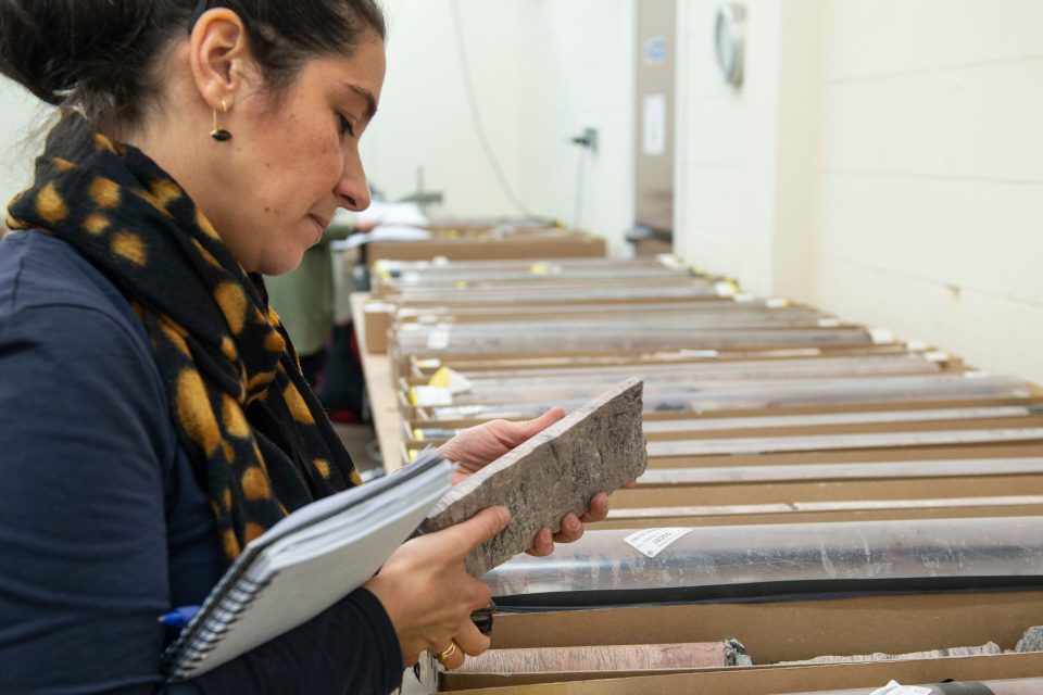 A woman carrying a notebook examines a piece of rock core