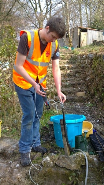 A man in a hi-vis orange jacket and blue jeans undertaking groundwater tests