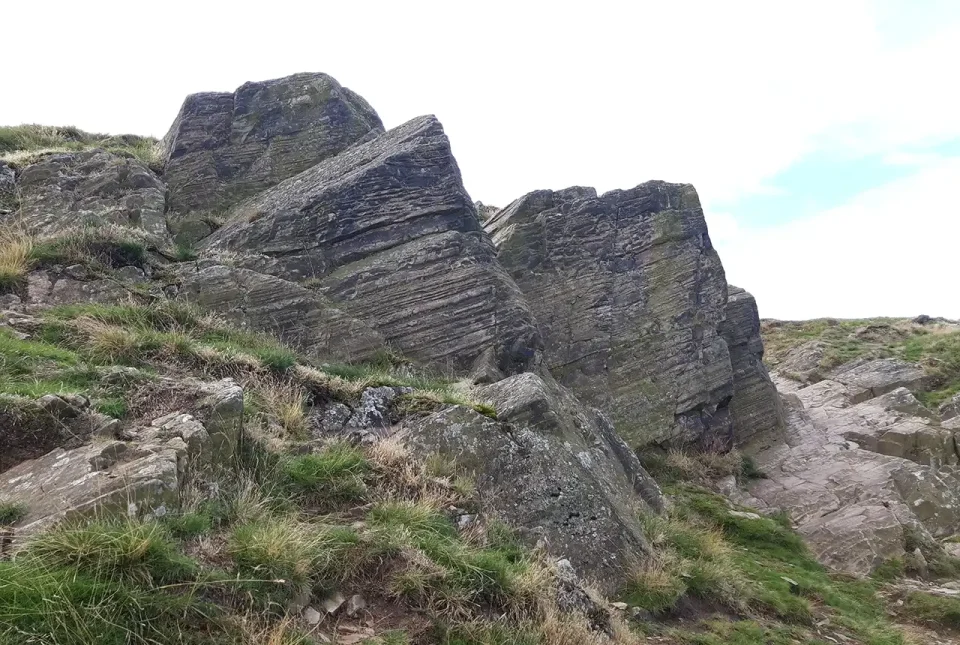 The ash from the volcanoes in the area would have settled under water to create layered deposits. This outcrop is on the same hill as Old John Tower. BGS © UKRI.