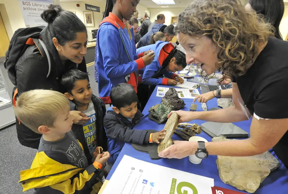 A geologist is explaining rock samples to young children. One of the children is touching the rock to explore its texture.