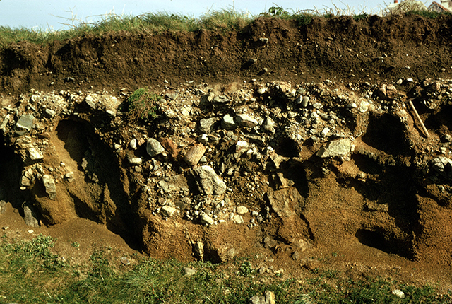 Superficial deposits can be very heterogeneous and challenging to predict. Here, a gravel and boulder rich raised beach deposit lies atop weathered gneiss bedrock in Guernsey, Channel Islands. This is overlain by a fine wind-blown cover sand.